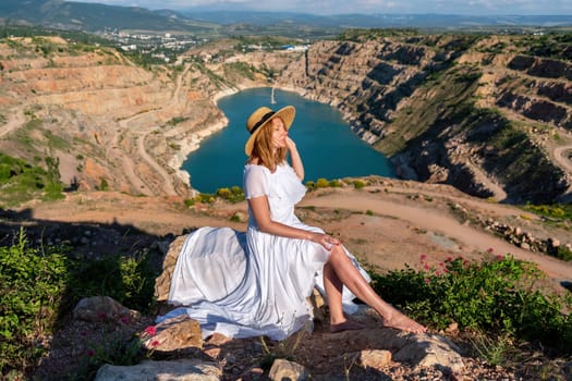 A woman in a white dress is sitting on a rock overlooking a body of water. The scene is serene and peaceful, with the woman enjoying the view and the calmness of the surroundings