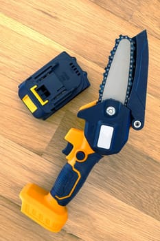 small accumulator chainsaw and battery on a wooden surface 