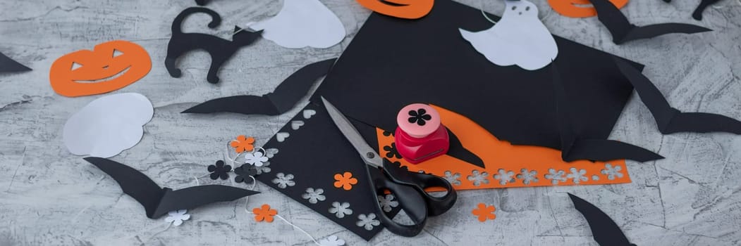 banner with paper decor for Halloween. carved orange pumpkin, jack-o'-lantern, white ghost, black cat. Preparation for the holiday, scissors and colored paper, paper garland. soft focus