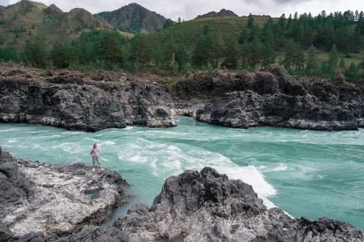 A solitary figure stands firmly on the rocks by a flowing, turquoise Katun river that is surrounded by lush greenery