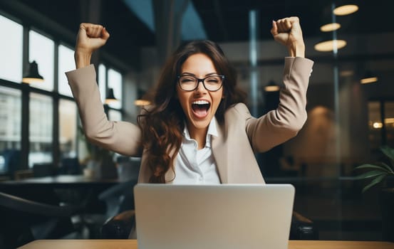 Happy overjoyed laughing businesswoman celebrating success raising his hands up while working on laptop sitting at his desk in the office
