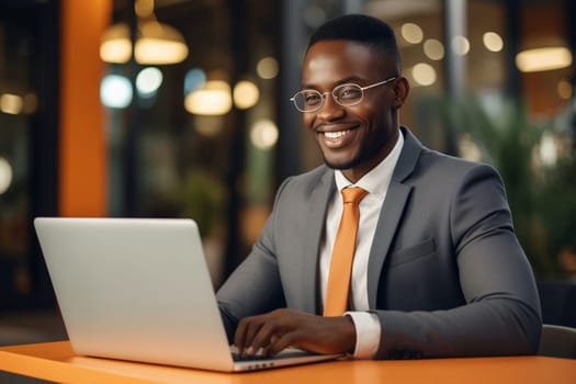 Happy successful African young businessman working on a laptop, smiling black male entrepreneur sitting in a cafe