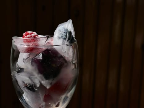 Glass with ice cubes with frozen berries and fruits close-up for a refreshing drink and preservation of seasonal vitamins raspberries, strawberries, cherries, blueberries, mulberries, blackberries