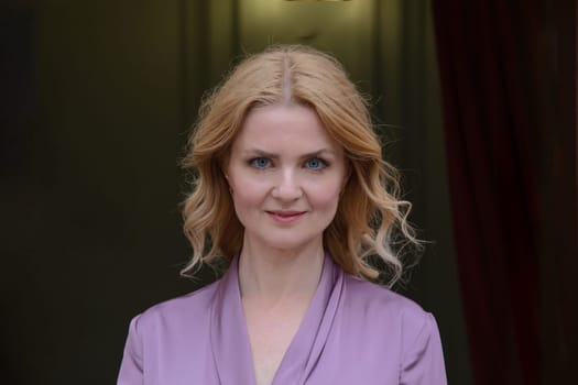 Image of a woman with long, beautiful hair in purple clothes, on the dark background of the apartment, looking into the camera.