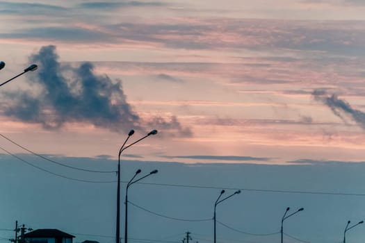 Streetlights stand in silhouette against a beautiful sunset sky with pink and grey clouds.