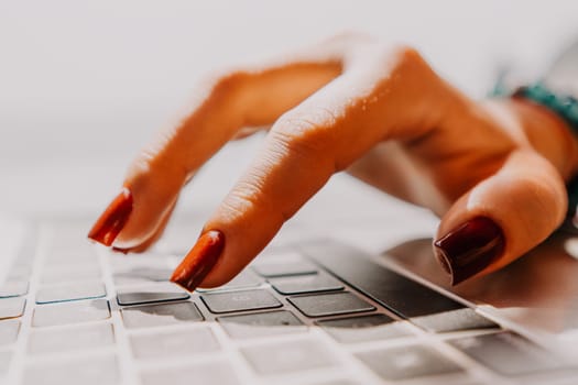 A hand with red nail polish types on a laptop keyboard.