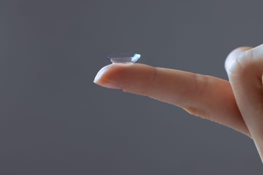 Close-up of finger holding contact lens, on grey background, concept of poor eyesight, astigmatism, myopia, hyperopia, treatment of deteriorating vision