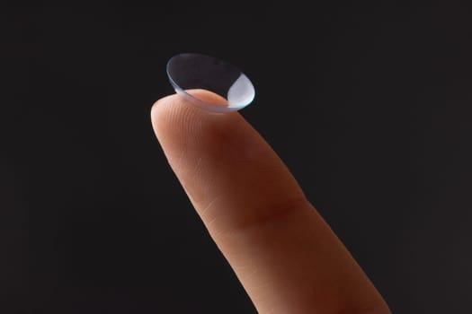 Close-up of finger holding contact lens, on grey background, concept of poor eyesight, astigmatism, myopia, hyperopia, treatment of deteriorating vision