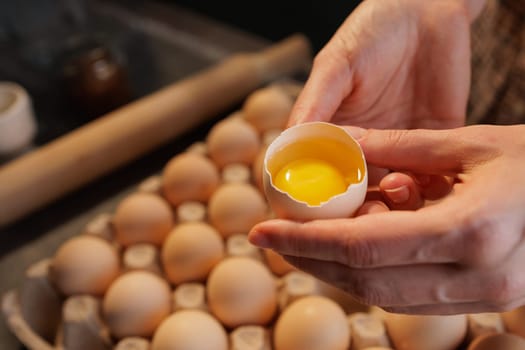 Close-up of female hands holding broken chicken egg on background of egg carton Close-up, healthy eating concept