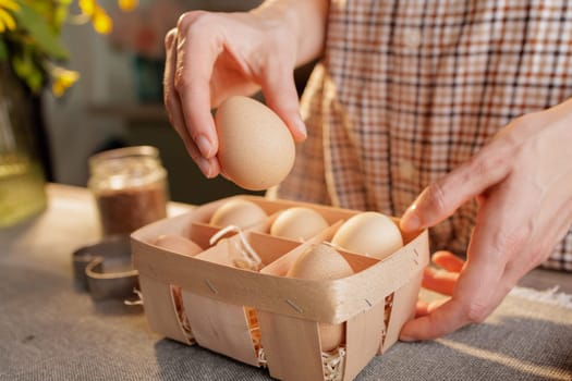 young woman takes chicken egg out of package close-up on kitchen table, home kitchen background, homemade baking concept