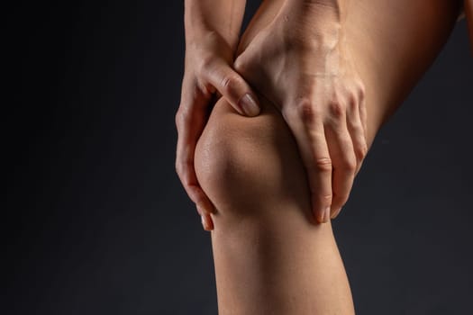 woman hands close up pressing on knee joint on dark background, knee pain concept, leg pain treatment