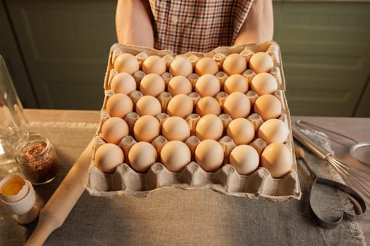 A man holds a large egg carton, with 30 eggs visible in it. In the background is a kitchen setting with utensils and jars. The focus is on the eggs in the carton.