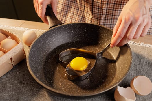 close-up of female hands holding a heart shape on a frying pan with a broken egg, heart-shaped fried egg