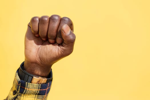 raised fist of a black man on an intense yellow background, concept of human rights struggle and lifestyle, copy space for text