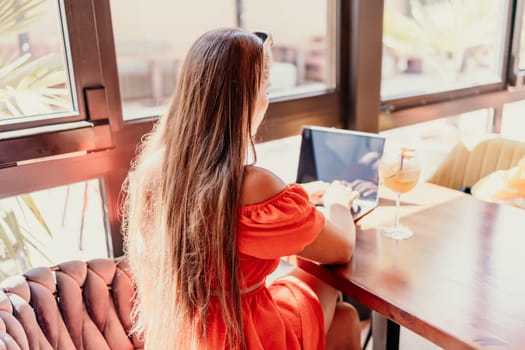 Woman works on laptop in a sunny cafe, glass of juice nearby. The setting is modern, with natural light illuminating the space. The image captures a moment of focused work