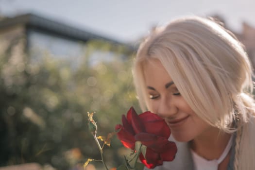 A woman is smelling a red rose. Concept of happiness and contentment, as the woman is enjoying the scent of the flower