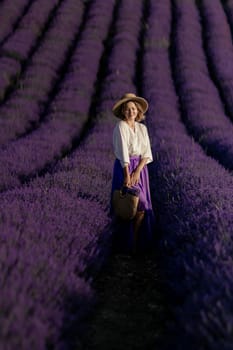 A woman is standing in a field of lavender flowers. She is wearing a straw hat and a blue skirt