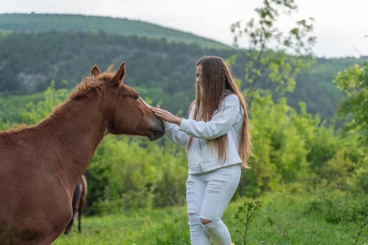 A woman is petting a brown horse in a grassy field. The scene is peaceful and serene, with the woman and the horse sharing a moment of connection