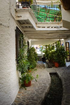 A rustic narrow alley with cobblestone paths, white walls, and flowing water surrounded by greenery, Alpujarras, granada, andalucia, espa a,