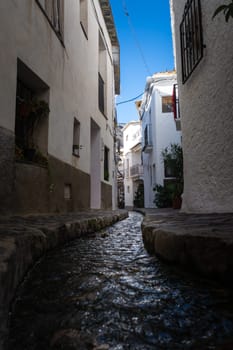 A narrow pathway with a small stream and white buildings on either side under a bright blue sky, Alpujarras, granada, andalucia, espa a,