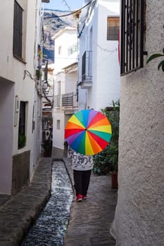 Person holding a colorful umbrella walking in a narrow alley with a water stream and white buildings, Alpujarras, granada, andalucia, espa a,