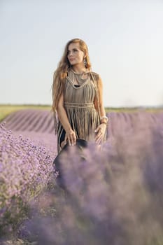 A woman is standing in a field of purple flowers, wearing a black dress and a black hat