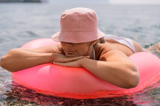 A woman is laying on a pink inflatable raft in the ocean. The scene is peaceful and relaxing, with the woman enjoying the water and the sun