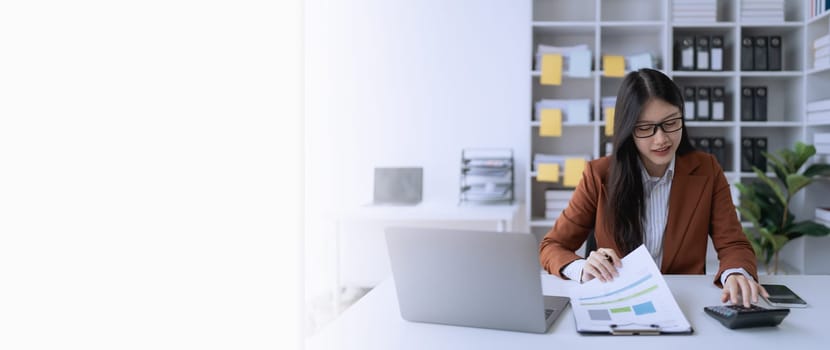 woman meticulously plans a finance audit, using a computer and calculator to review budget documents and ensure accuracy.