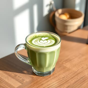 A beautiful matcha latte sits on a wooden table, showcasing delicate latte art shaped like a heart. Sunlight filters through, creating a warm and inviting atmosphere.