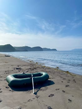 An inflatable boat moored on the shore of a lake. A green boat on the sandy shore of a pond. Fishing, a man's hobby. High quality photo