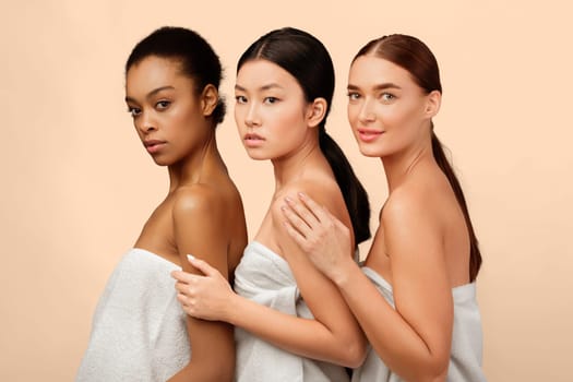 Beauty And Spa. Three Sensual Girls In Bath Towels Posing Looking At Camera On White Background. Studio Shot