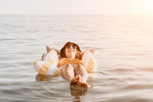 A woman wearing sunglasses floats on an inflatable ring in calm water. She is smiling and appears relaxed.
