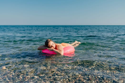 A woman is floating on a pink inflatable raft in the ocean. The water is calm and the sky is clear. The woman is relaxed and enjoying her time in the water