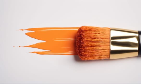 An orange paintbrush lays on a white surface with a streak of orange paint created by the brush.