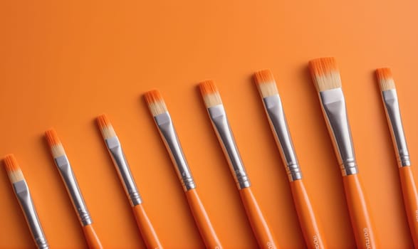 A group of paintbrushes with orange handles are arranged in a row on an orange background