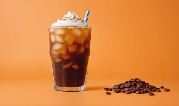 A glass of iced coffee sits on an orange background. The coffee is topped with whipped cream and a straw. A small pile of coffee beans lies to the right of the glass.
