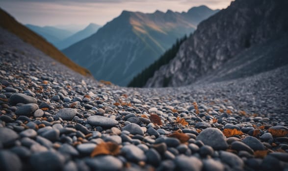 A shallow depth of field shot shows a rocky path leading up toward a mountain range. The path is made of gray pebbles and the mountains are a muted blue-grey.