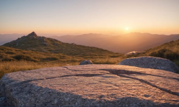 A large, flat rock sits on a grassy mountain peak. The sun is setting behind distant hills, casting a warm glow over the landscape.