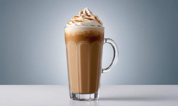 A tall glass mug filled with iced coffee is sitting on a white table. The coffee is topped with whipped cream and drizzled with caramel. The background is a light blue.