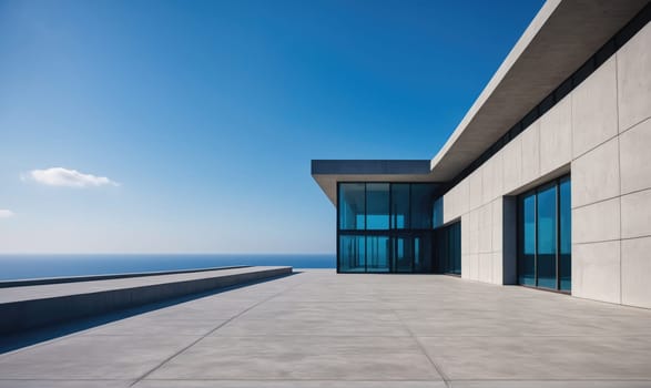 A large, modern house with large windows and a concrete patio overlooks the ocean. The sky is blue with a few wispy clouds