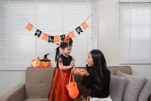 A mother and daughter enjoy Halloween festivities, surrounded by decorations and costumes, creating a warm and joyful family atmosphere.