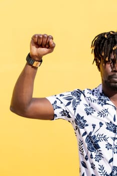 vertical photo of an attractive young black man with raised fist on an intense yellow background, concept of human rights struggle and lifestyle, copy space for text