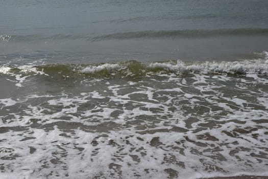 Beautiful landscape - turquoise colored sea water, sand, sky. The waves are on the sea to the shore. The Beach And Splashing Waves