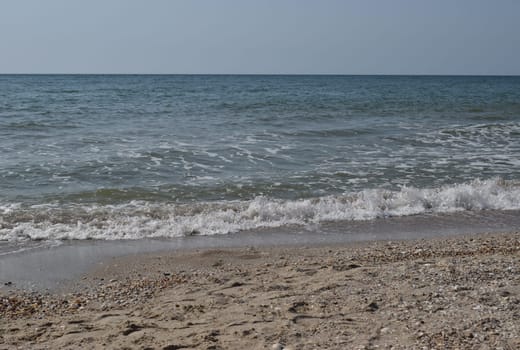 Beautiful landscape - turquoise colored sea water, sand, sky. The waves are on the sea to the shore. The Beach And Splashing Waves