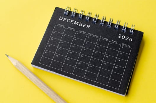 Top view of December 2026 calendar on black notepad with yellow background. Calendar concept.