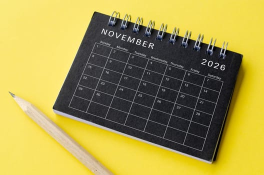 Top view of November 2026 calendar on black notepad with yellow background. Calendar concept.