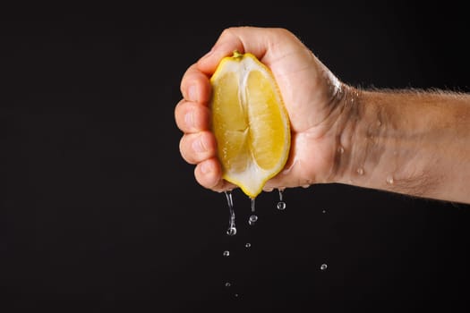 A hand squeezing a lemon, with juice dripping down. The background is black, highlighting the freshness of the lemon and the action of squeezing.