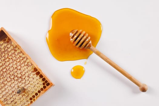 spoon with spilled honey and bee honeycomb on white background, top view, beekeeping concept