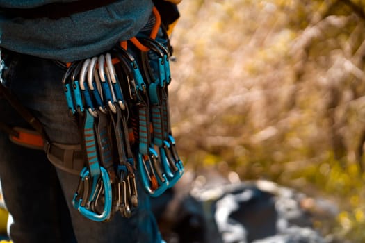 Young man, traveler is training outdoor with climbing equipment, safety belts, carabiners, rope, quickdraws close-up. Backpacker is involved in active sports, mountaineering and rock climbing.