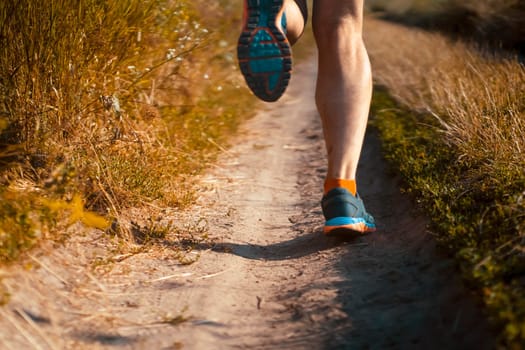 Athlete runner legs running on a close-up of a trail across a field on a shoe. Fitness and warm-up, young man with sun effect in the background.